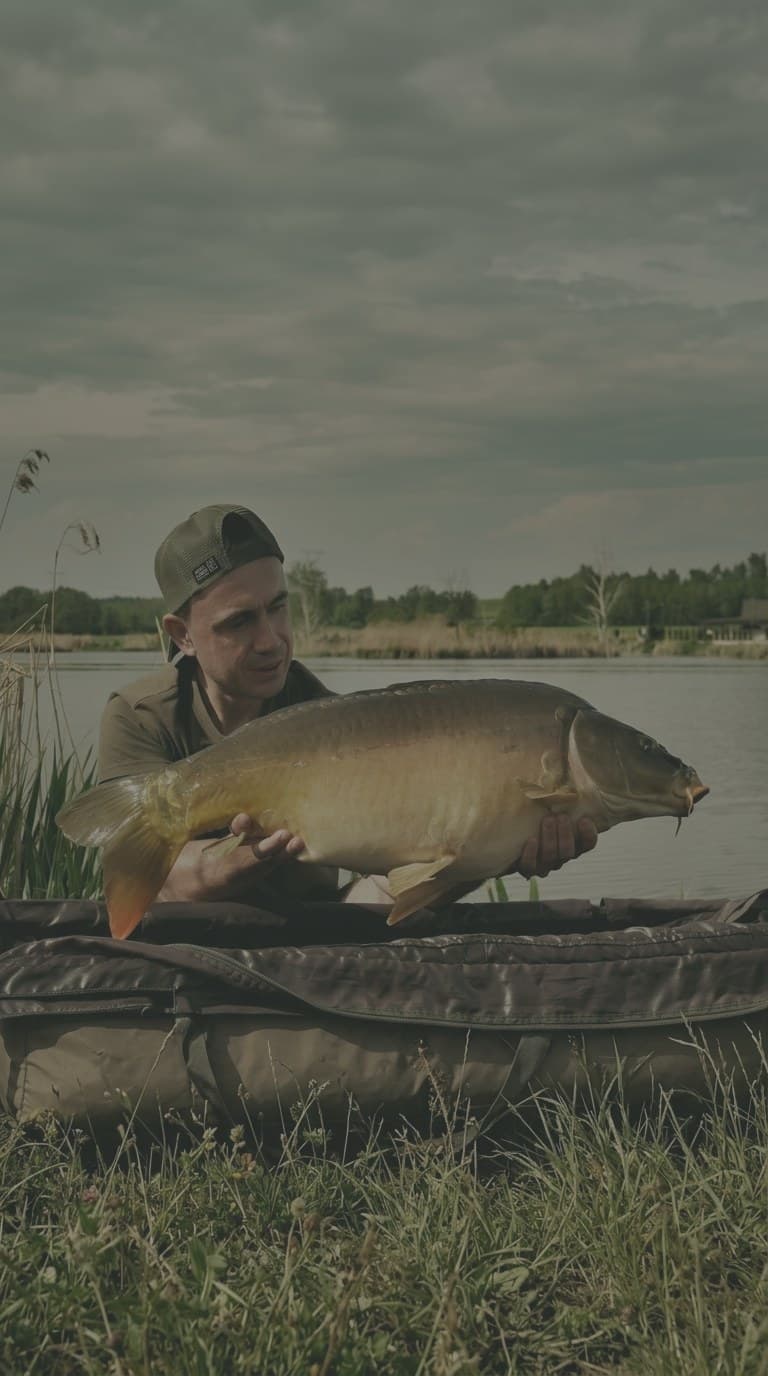 Wędkarz z dorodnym karpiem nad wodą łowiska Big Fish Lake